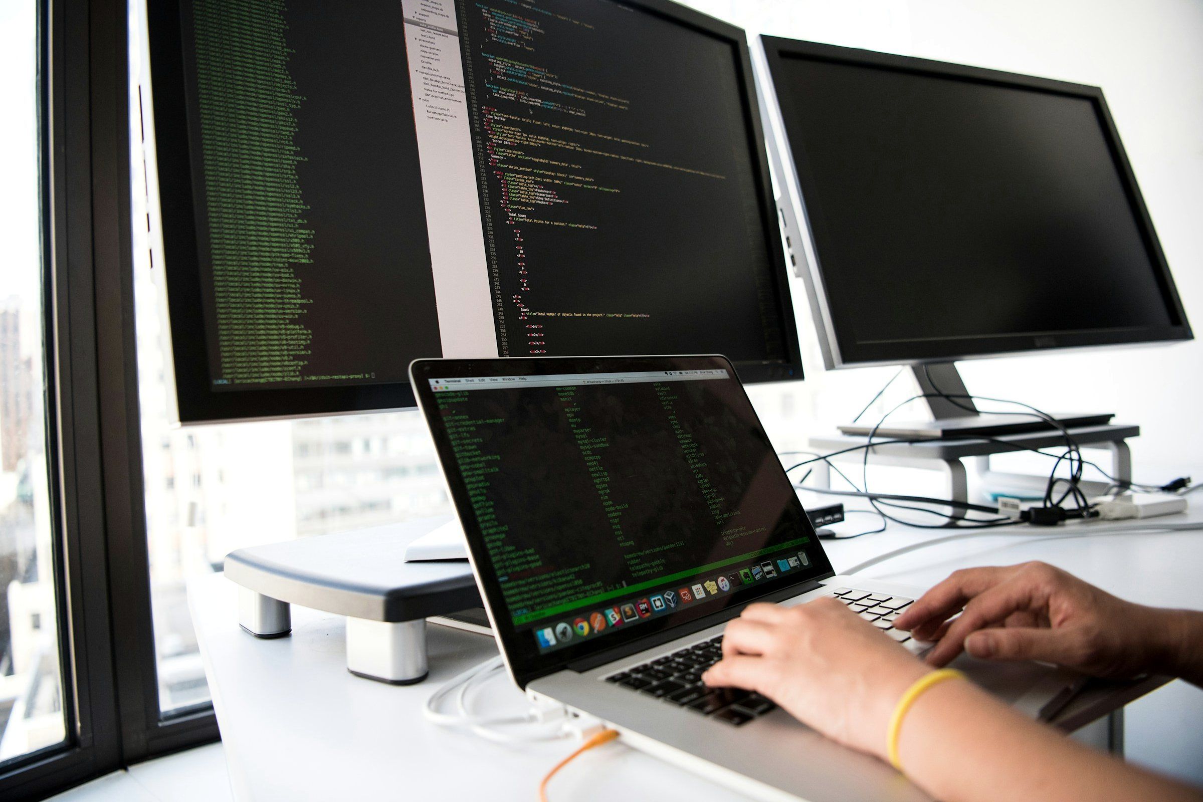 Hands on a laptop in front of screens with source code