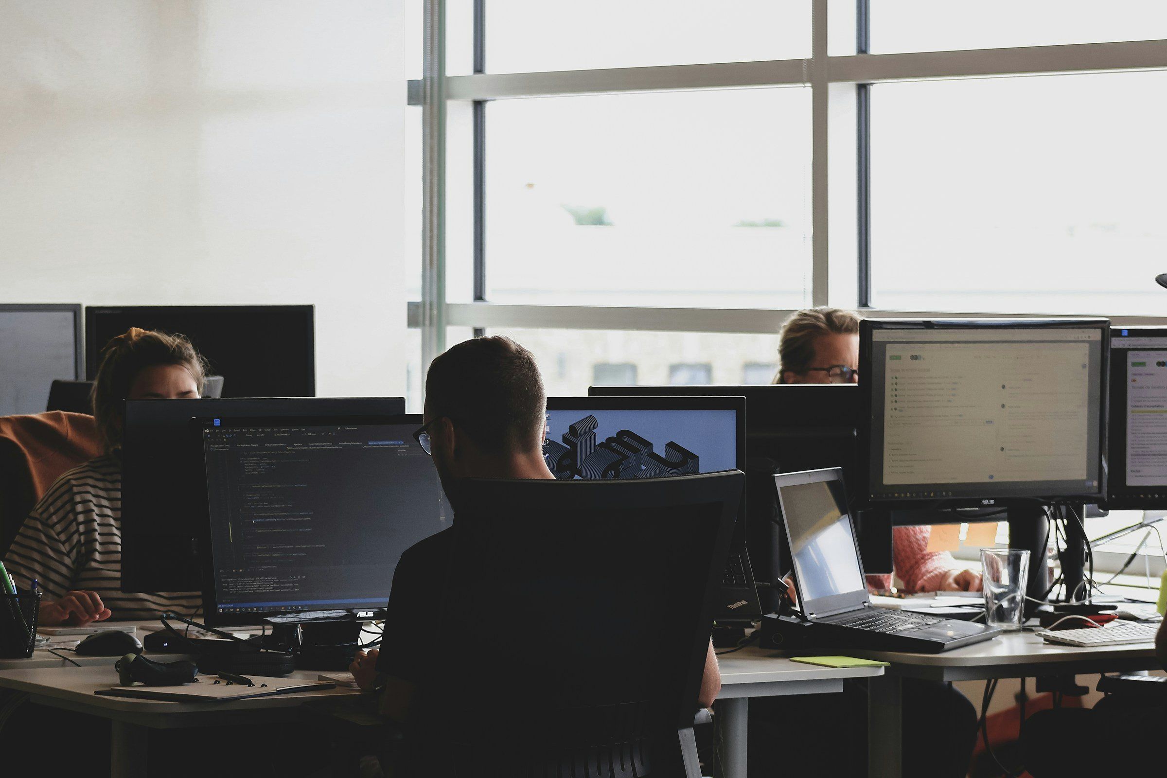 Team working at screens in a bright office, seen from behind